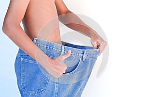 Young man in loose jeans on white background. Weight loss concept.