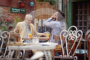 The young man lost a game of chess while playing with an elderly friend at the bar. Leisure, bar, friendship, outdoor