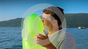 Young man lovingly inflates an inflatable swimming ring for his kids on a sunset beach. Tourism, the joy of summertime