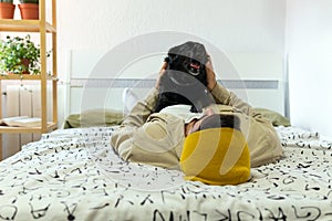 Young man lying in bed with his dog on top yawning