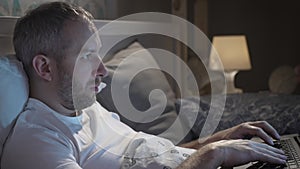 Young man lying in the bed with laptop before sleeping