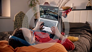 Young man lying on the bed playing video game on the laptop