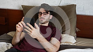 Young man lying in bed and reading ebook