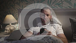 Young man lying in the bed with smartphone before sleeping.