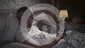 Young man lying in the bed with smartphone before sleeping.
