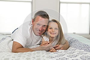 Young man lying on bed together with adorable 7 years old little girl playing happy at home in family father and daughter love li