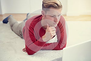 Young man lying on floor and looking at laptop