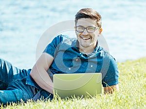 Young man lying on grass and using laptop