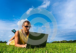 Young man lying on the grass and working with laptop