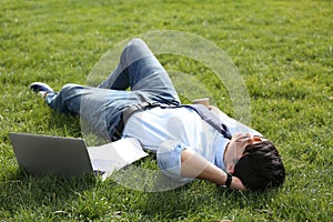 Young man lying on green lawn in park