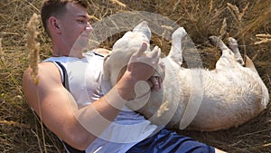 Young man lying on meadow and caressing his labrador. Male owner playing with golden retriever at nature. Love and