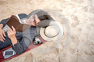 Young man lying on sandy beach and reading his notebook