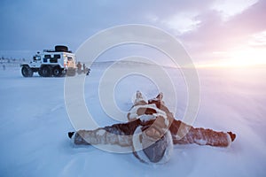 Young man lying on snow dressed in Nenets warm clothes at sunset, in desert of Siberia.