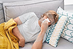 Young man lying on sofa using napkin at home