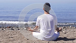 Young man makes meditation in lotus pose on sea / ocean beach, harmony and contemplation.