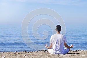 Young man makes meditation in lotus pose on sea / ocean beach, harmony and contemplation. Boy practicing yoga at sea resort at her