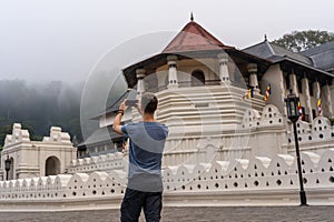 The young man makes photo with his phone of the Sri Dalada Maligawa temple in Kandy, Sri Lanka