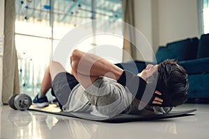 Young man making abdominal exercises on yoga mat in living room at home. Fitness, workout and traning at home concept