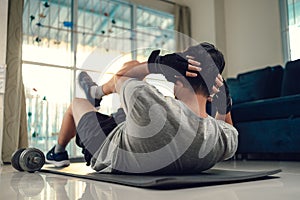 Young man making abdominal exercises on yoga mat in living room at home. Fitness, workout and traning at home concept