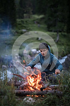 Young man making fire while camping outdoors