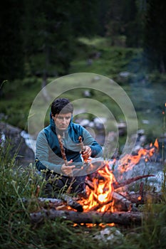 Young man making fire while camping outdoors