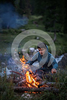 Young man making fire while camping outdoors