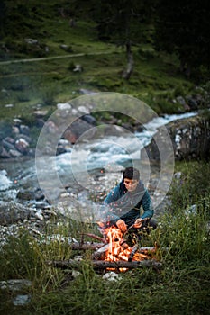 Young man making fire while camping outdoors