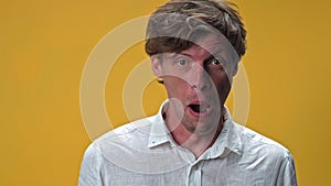 Young man making funny silly facial emotions isolated on yellow background. Weird dorky face of a handsome young man in