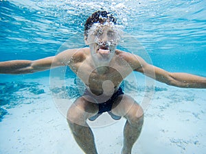 Young man making grimaces underwater. Clear blue water