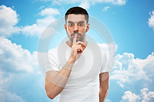 Young man making hush sign over blue sky