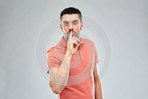 Young man making hush sign over gray background