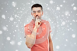 Young man making hush sign over snow background