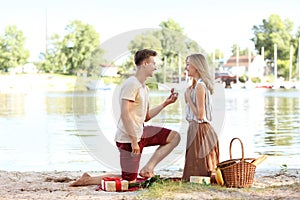 Young man making proposal to his girlfriend on romantic date near river