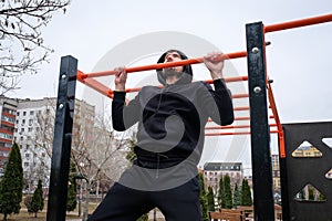 Young man making pull-up exercises on the crossbar outdoors. Fitness, sport, exercise, training and healthy lifestyle concept