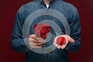 Young man making wedding proposal holding one red rose and box with engagement ring