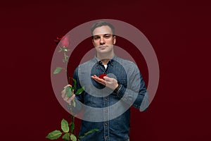 Young man making wedding proposal holding one red rose and box with engagement ring. Concept of love