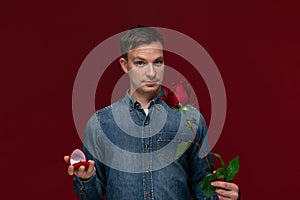 Young man making wedding proposal holding one red rose and box with engagement ring. Concept of love