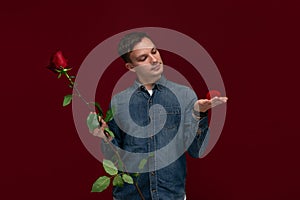 Young man making wedding proposal holding one red rose and box with engagement ring. Concept of love