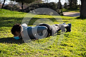 Young man with mask doing push-ups in a park. training and health with covid