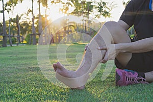 Young man massaging his painful calf ache from jogging and running outside at the park. Sport and exercise concept