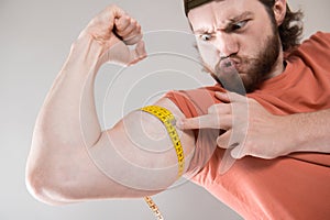 Young man measuring biceps, muscles of his arm with a yellow tape measure