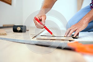 Young man measuring and marking laminate floor tile for cutting installing laminate flooring