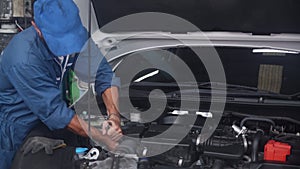 Young man is mechanic repairing engine of car in the garage, auto service, worker fix and adjusting part of automobile.