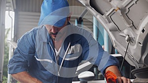 Young man is mechanic repairing engine of car in the garage, auto service, worker fix and adjusting part of automobile.