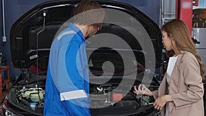 Young man mechanic talking with customer for examining trouble and repairing engine of car in the garage.