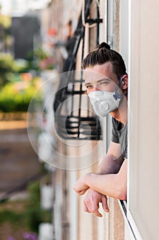 Young man in a medical mask looks out of the window from home, is in quarantine of the coronavirus 2020 epidemic, covid-19