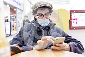 Young man in a medical mask in a shopping center with a phone in his hands. Coronavirus pandemic