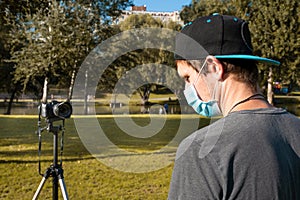 A young man in a medical protective mask on the street records a video blog on the camera. Online communication, consultations,