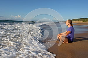 Young man meditates on beach in lotus pose