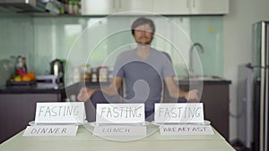 A young man meditates in frint of a table with empty plates on which writtings ` fasting` are placed. Yoga diet